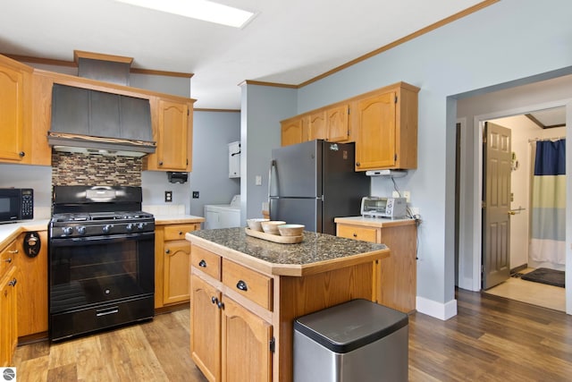 kitchen with washing machine and dryer, wood finished floors, custom exhaust hood, black appliances, and ornamental molding