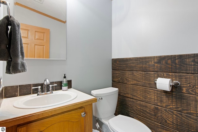 half bathroom featuring vanity, ornamental molding, and toilet