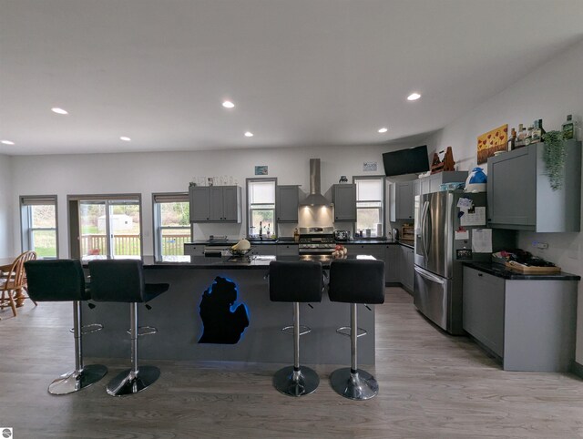 kitchen with dark countertops, a kitchen breakfast bar, light wood-style flooring, wall chimney exhaust hood, and stainless steel appliances