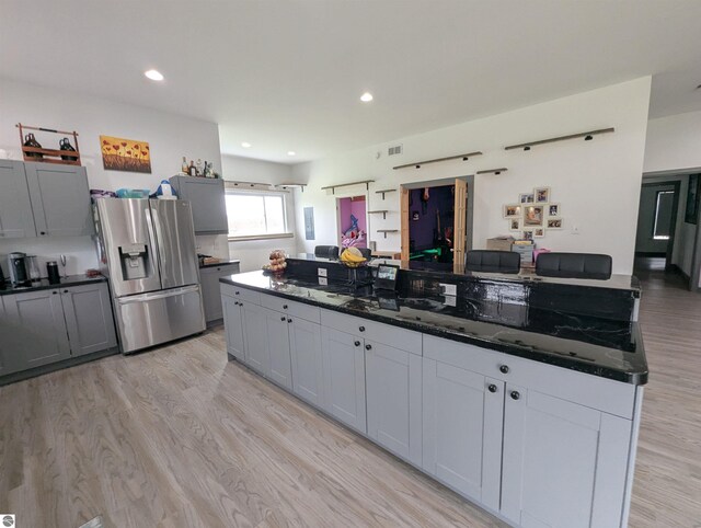kitchen with dark stone counters, stainless steel refrigerator with ice dispenser, visible vents, and light wood-type flooring
