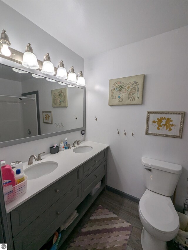 full bathroom featuring a sink, double vanity, toilet, and wood finished floors