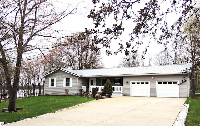 single story home featuring concrete driveway, covered porch, a front yard, metal roof, and an attached garage