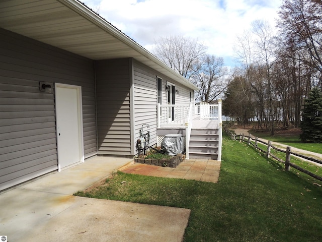 property entrance featuring fence, a wooden deck, and a lawn