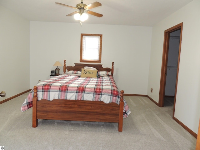 bedroom with baseboards, ceiling fan, light carpet, and a walk in closet