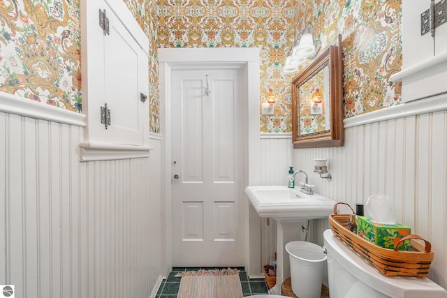 half bathroom featuring toilet, wallpapered walls, and wainscoting