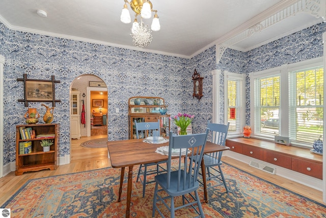 dining space with visible vents, crown molding, arched walkways, wood finished floors, and a chandelier