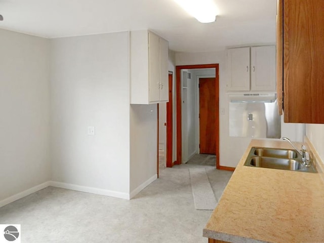 kitchen featuring a sink, baseboards, under cabinet range hood, and light countertops