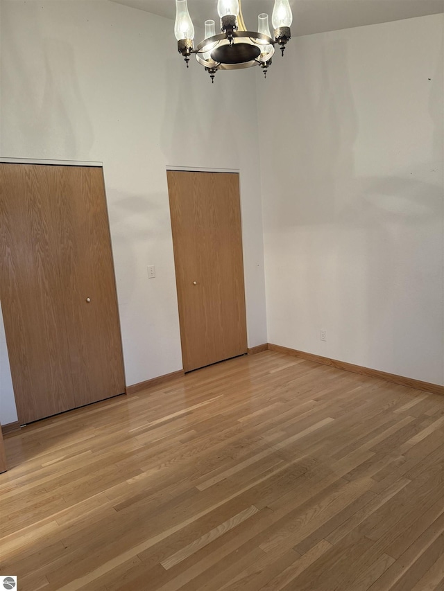 unfurnished dining area with baseboards, a notable chandelier, and wood finished floors