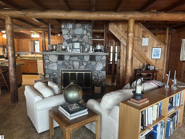 carpeted living room featuring wood ceiling, a fireplace, a sink, beamed ceiling, and wooden walls