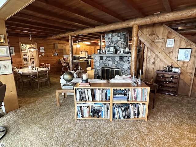 carpeted living area with a stone fireplace, wooden walls, and beamed ceiling