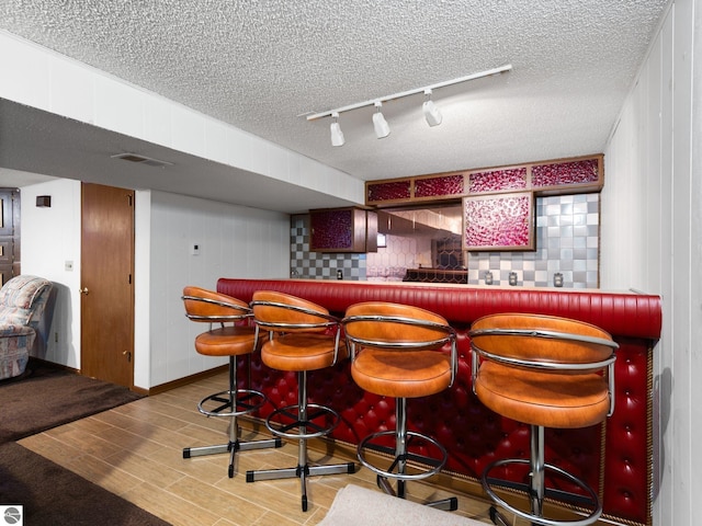 bar featuring a bar, rail lighting, a textured ceiling, and visible vents