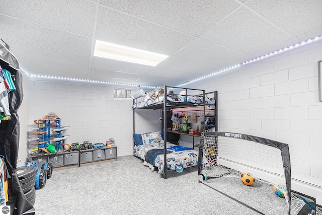 carpeted bedroom with a paneled ceiling and concrete block wall