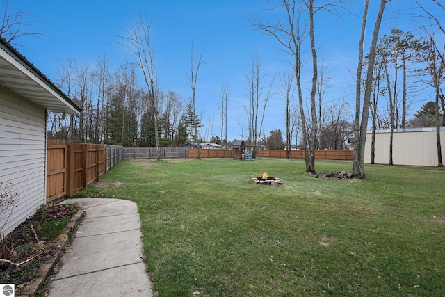 view of yard featuring a fire pit, a fenced backyard, and a playground