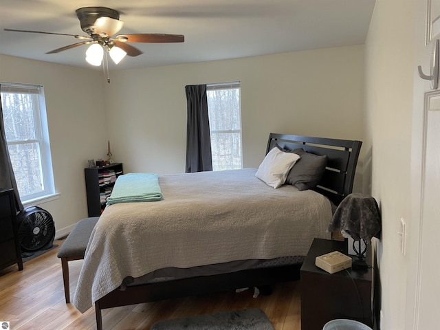 bedroom with a ceiling fan, light wood finished floors, and multiple windows