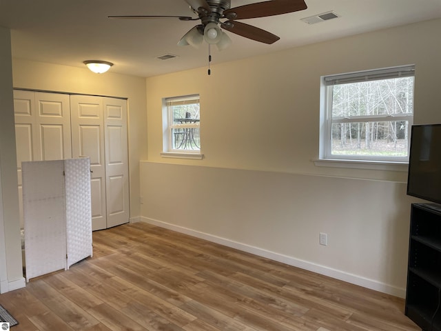 unfurnished bedroom with baseboards, multiple windows, wood finished floors, and visible vents