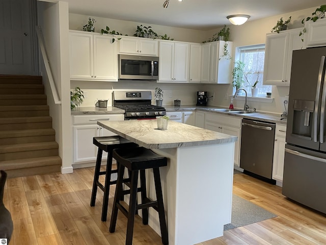 kitchen with a sink, light wood finished floors, light countertops, stainless steel appliances, and a kitchen island