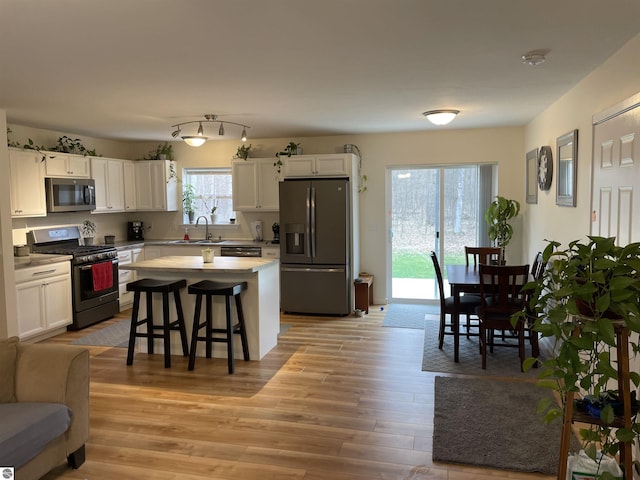 kitchen with stainless steel appliances, white cabinetry, light wood-style flooring, and a kitchen bar
