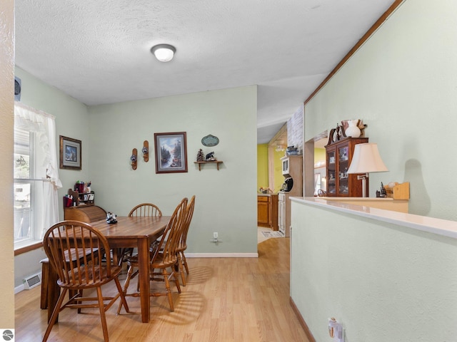 dining space with a textured ceiling, baseboards, visible vents, and light wood-type flooring