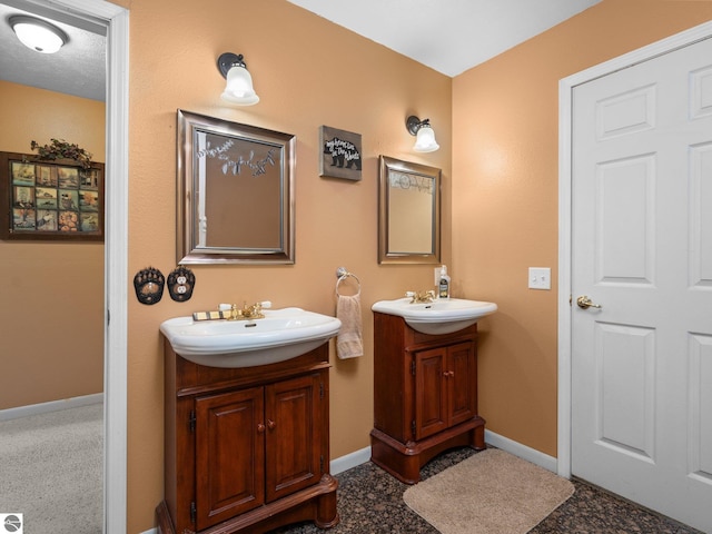 bathroom with baseboards, a sink, and two vanities