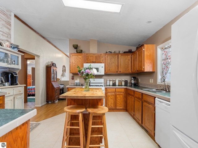 kitchen featuring a kitchen island, a sink, lofted ceiling, a breakfast bar, and white appliances