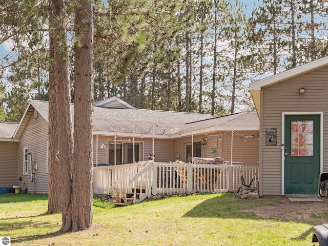 back of house with a lawn, a shingled roof, and a wooden deck