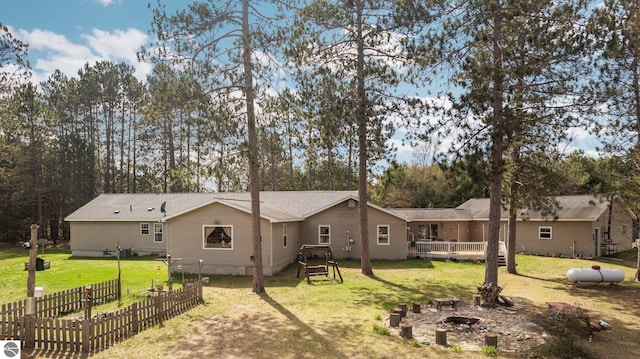 back of property with a lawn, fence, a fire pit, and a deck