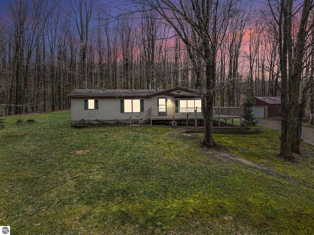manufactured / mobile home with a garage, a wooden deck, a view of trees, an outbuilding, and a lawn