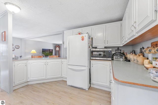 kitchen with freestanding refrigerator, light wood-style floors, white cabinetry, stainless steel microwave, and a textured ceiling