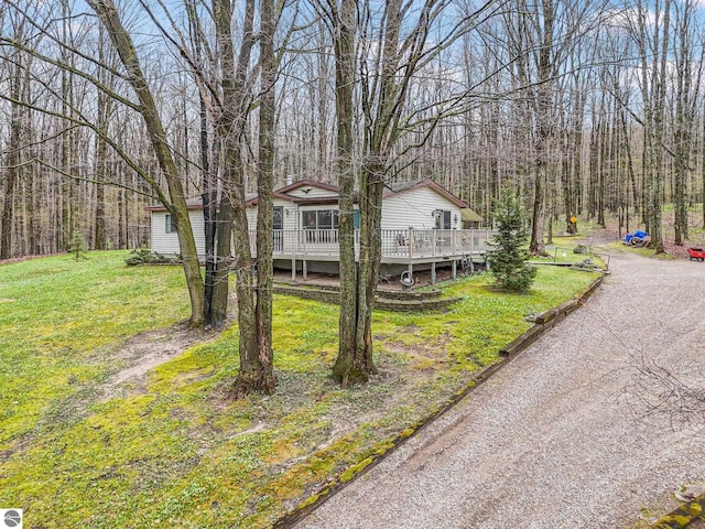 view of front facade featuring a wooded view, a wooden deck, and a front lawn