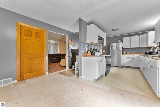 1981 S Lake Mitchell Dr, Cadillac, MI 49601 - kitchen with visible vents, freestanding refrigerator, black microwave, gas range, and white cabinets
