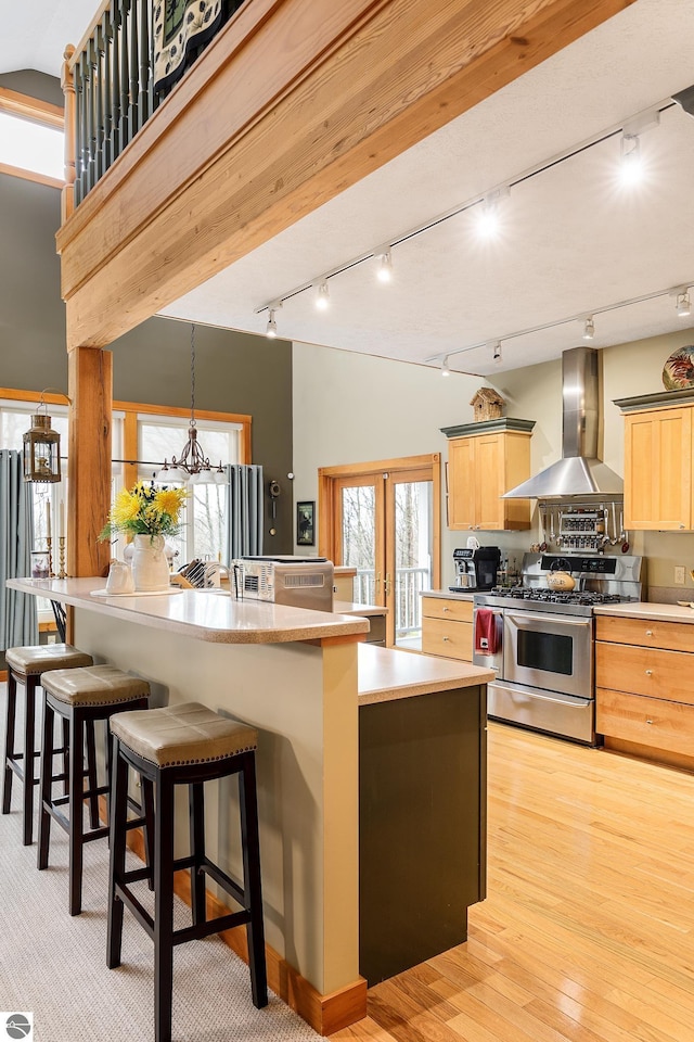 kitchen with track lighting, an inviting chandelier, a kitchen bar, wall chimney exhaust hood, and stainless steel range with gas stovetop