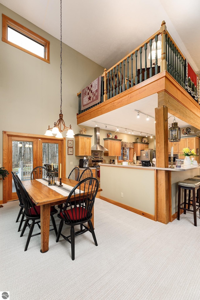 dining area featuring light colored carpet, rail lighting, a chandelier, baseboards, and a towering ceiling