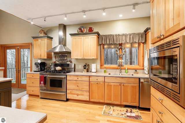 kitchen featuring wall chimney range hood, a sink, light countertops, rail lighting, and stainless steel appliances