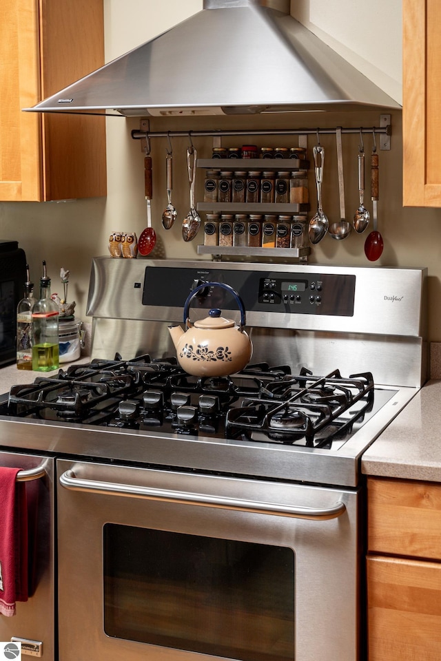 kitchen with gas stove, light countertops, brown cabinetry, decorative backsplash, and range hood