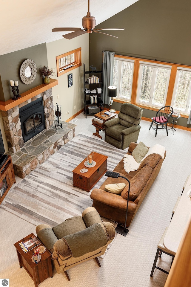 living area featuring a ceiling fan, baseboards, a stone fireplace, high vaulted ceiling, and carpet flooring