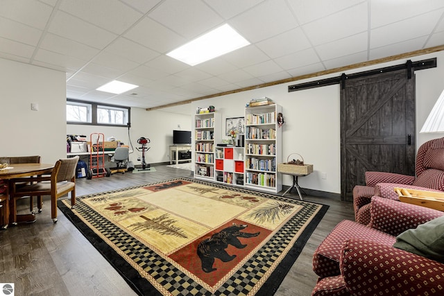 living room with a barn door, baseboards, wood finished floors, and a paneled ceiling