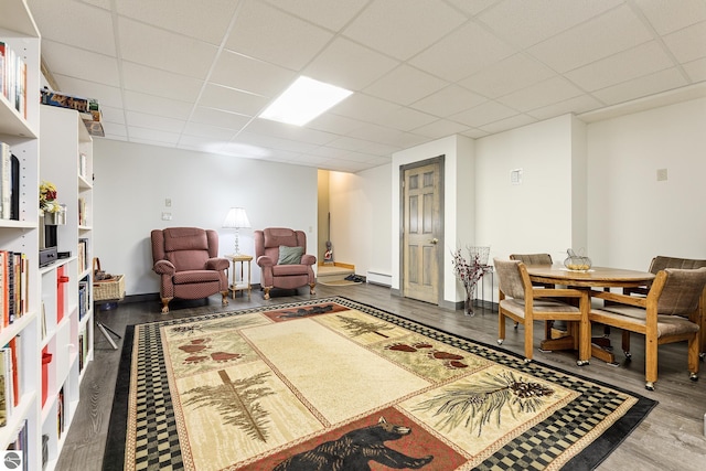 living area featuring baseboards, a baseboard radiator, a paneled ceiling, and wood finished floors