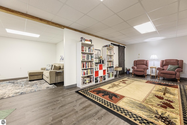 living room featuring baseboards, a barn door, a paneled ceiling, and wood finished floors