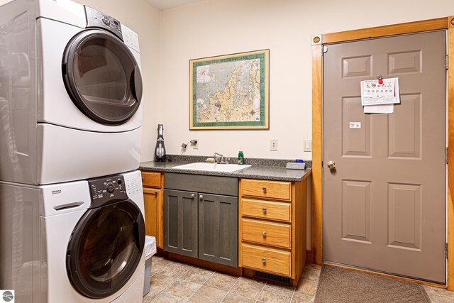 laundry area featuring a sink, cabinet space, and stacked washer / dryer