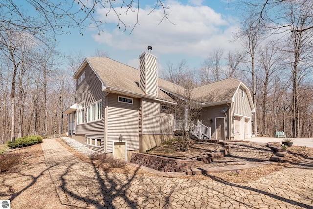 rear view of house featuring a shingled roof, a chimney, and concrete driveway