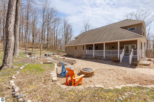 rear view of property featuring a porch, a fire pit, and roof with shingles