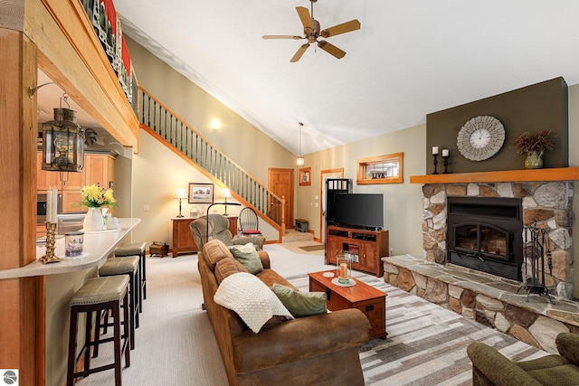 living area featuring lofted ceiling, a stone fireplace, ceiling fan, stairway, and light colored carpet