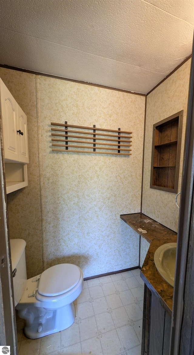 half bathroom with toilet, vanity, a textured ceiling, tile patterned floors, and wallpapered walls