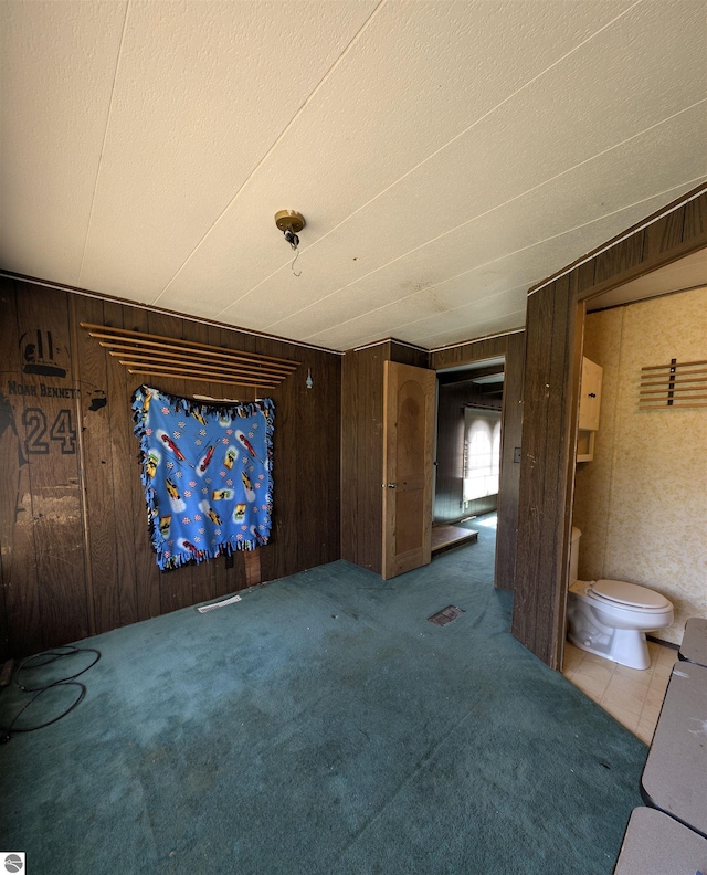 unfurnished living room featuring a textured ceiling, wooden walls, and carpet floors