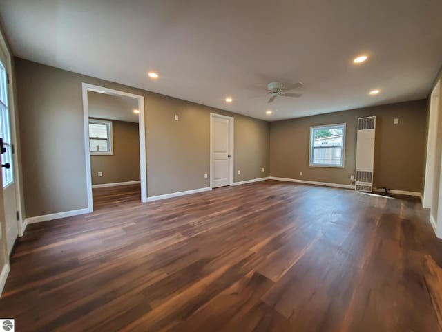 interior space featuring a ceiling fan, baseboards, dark wood-type flooring, and a heating unit