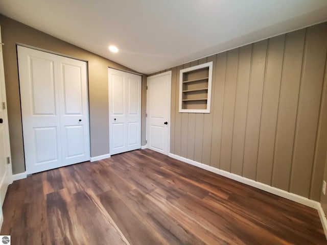 unfurnished bedroom featuring vaulted ceiling, baseboards, multiple closets, and dark wood finished floors