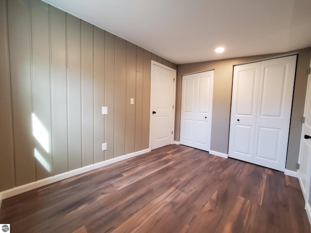 unfurnished bedroom featuring two closets, recessed lighting, baseboards, and dark wood finished floors