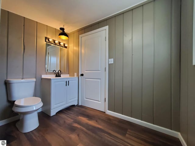 half bath with vanity, toilet, baseboards, and wood finished floors
