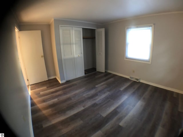 unfurnished bedroom with crown molding, dark wood-style floors, baseboards, and a closet
