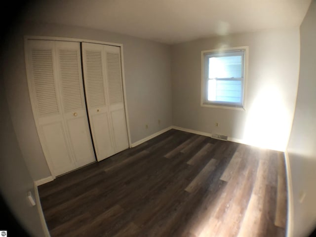 unfurnished bedroom with dark wood-style flooring, a closet, and baseboards
